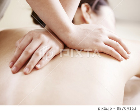 close-up of hands of a masseuse massaging back of a young asian woman 88704153