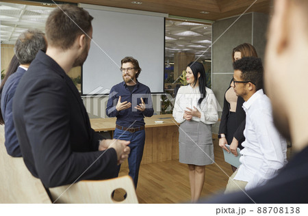 Creative business coach speaking to team of entrepreneurs who are standing in office around him 88708138