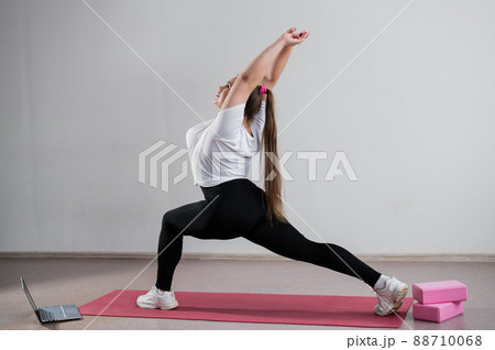 Young Plus Size Woman Stretching At Home Online. Flexible girl practices yoga and watches an online course on a laptop 88710068