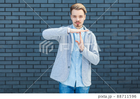 Time. Portrait of serious handsome young blonde man in casual style standing with timeout gesture hand and looking at camera with calm face. indoor studio shot on brick wall background. 88711596