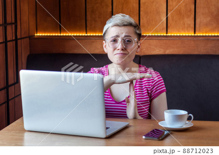Portrait of warning sad attractive young girl freelancer with blonde short hair is sitting in cafe and looking at camera with raised arms and showing pause gesture, indoor, lifestyle Portrait of warning sad attractive young girl freelancer with blonde short hair is sitting in cafe and looking at camera with raised arms and showing pause gesture, indoor, lifestyle 88712023