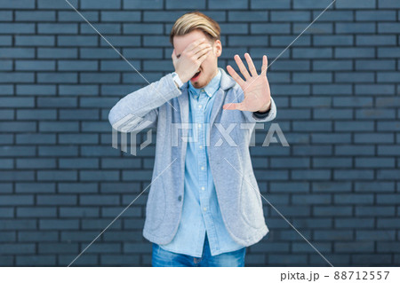 I don't want to look at this. Portrait of ignoring handsome young blonde man in casual style standing, closed his eye and showing stop sign gesture. indoor studio shot on brick wall background. I don't want to look at this. Portrait of ignoring handsome young blonde man in casual style standing, closed his eye and showing stop sign gesture. indoor studio shot on brick wall background. 88712557