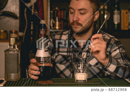 Focused bartender preparing alcoholic cocktail White Russian behind bar counter 88712908