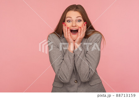 Portrait of amazed young brunette woman in business suit keeping hands on face and shouting in surprise, expressing genuine astonishment, shock reaction. indoor studio shot isolated on pink background Portrait of amazed young brunette woman in business suit keeping hands on face and shouting in surprise, expressing genuine astonishment, shock reaction. indoor studio shot isolated on pink background 88713159
