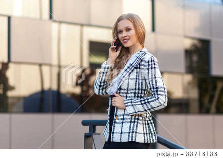 Portrait of stunning beautiful blond lady in stylish plaid jacket talking on cellphone, looking aside with charming toothy smile, successful rich businesswoman having conversation on phone, outdoor Portrait of stunning beautiful blond lady in stylish plaid jacket talking on cellphone, looking aside with charming toothy smile, successful rich businesswoman having conversation on phone, outdoor 88713183