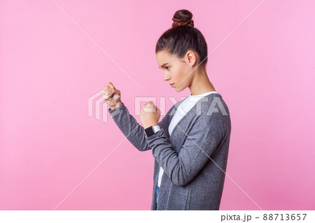 Side view of brave teenage girl with bun hairstyle in casual clothes standing in defensive posture with raised fists, ready to punch, looking aggressive and confident. studio shot, pink background Side view of brave teenage girl with bun hairstyle in casual clothes standing in defensive posture with raised fists, ready to punch, looking aggressive and confident. studio shot, pink background 88713657