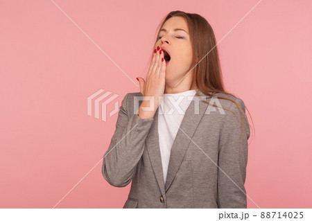 Portrait of sleepy exhausted young woman in business suit yawning lovely, covering mouth with hand, feeling lazy fatigued after work, needs rest. indoor studio shot isolated on pink background 88714025