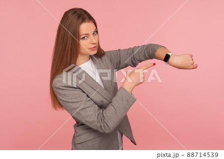 Rush, hurry up to come in time. Portrait of worried busy lady in business suit pointing to watch on her wrist and looking displeased, reminding about late hour. studio shot isolated on pink background 88714539