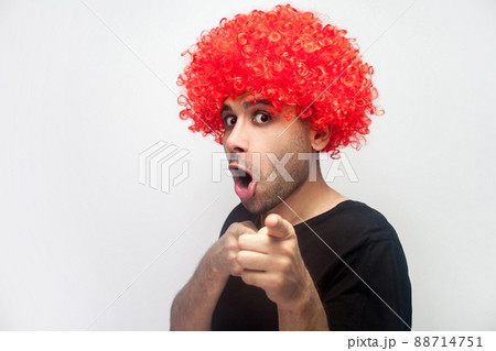 Portrait of funny surprised man with bristle and curly red wig pointing to camera and looking with shocked amazed hilarious face expression. indoor studio shot isolated on white background 88714751