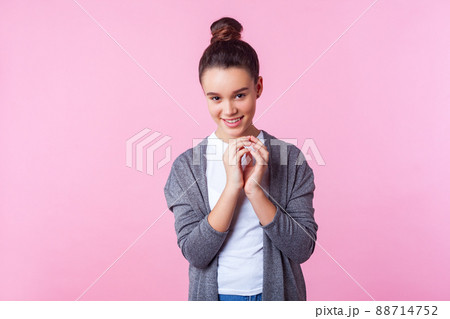 Portrait of funny playful brunette teenage girl with bun hairstyle in casual clothes grinning at camera with cunning sly expression, making tricky plan to prank friend. studio shot pink background Portrait of funny playful brunette teenage girl with bun hairstyle in casual clothes grinning at camera with cunning sly expression, making tricky plan to prank friend. studio shot pink background 88714752