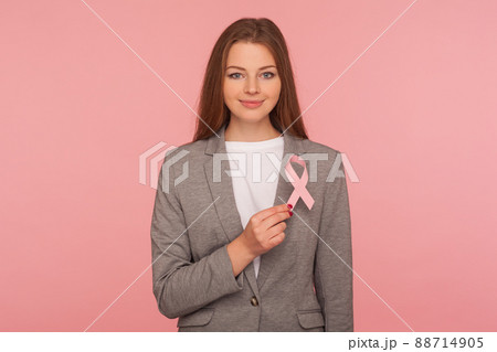 Female healthcare, medical insurance. Portrait of attractive positive businesswoman in elegant suit jacket holding pink ribbon, symbol of breast cancer awareness. indoor studio shot, pink background 88714905