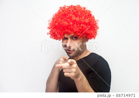 Portrait of funny positive man with bristle and red wig pointing to camera and winking playfully, flirting and getting acquaintance, asking for a date. studio shot, white background 88714971