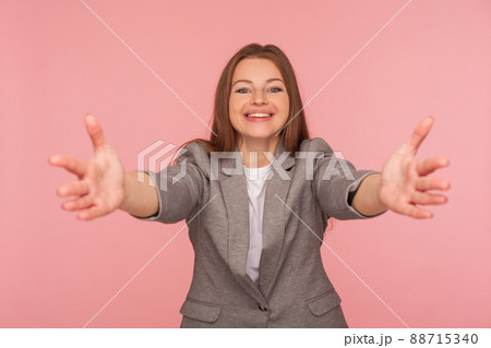 Free hugs. Portrait of joyful young woman in business suit keeping hands wide open, gesturing come here and smiling sincerely with welcoming expression. studio shot isolated on pink background 88715340