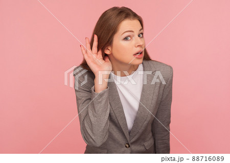 Portrait of curious nosy young woman in business suit holding hand near ear, listening carefully intently to interesting gossip, expressing amazement. indoor studio shot isolated on pink background Portrait of curious nosy young woman in business suit holding hand near ear, listening carefully intently to interesting gossip, expressing amazement. indoor studio shot isolated on pink background 88716089