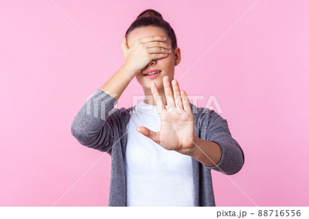 No, i don't want to look. Portrait of brunette teenage girl with bun hairstyle in casual clothes covering eyes and showing stop gesture, frightened or shocked of shameful content. indoor studio shot No, i don't want to look. Portrait of brunette teenage girl with bun hairstyle in casual clothes covering eyes and showing stop gesture, frightened or shocked of shameful content. indoor studio shot 88716556