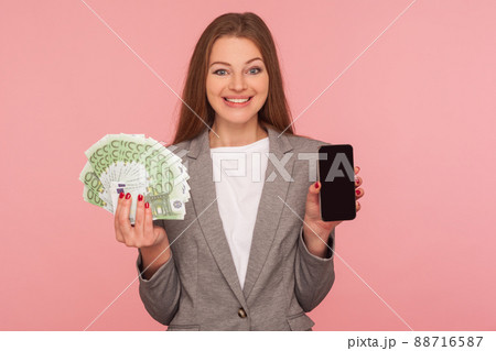 Loan application, apply online. Portrait of happy smiling businesswoman in suit jacket holding euro banknotes and cellphone, satisfied with mobile banking. studio shot isolated on pink background Loan application, apply online. Portrait of happy smiling businesswoman in suit jacket holding euro banknotes and cellphone, satisfied with mobile banking. studio shot isolated on pink background 88716587