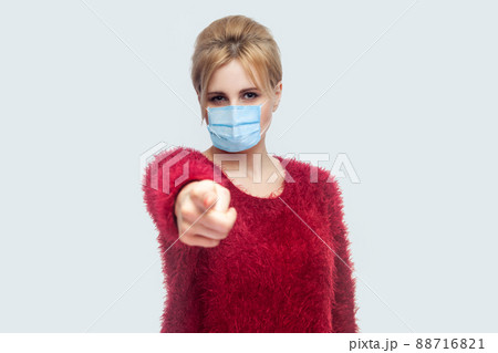 Portrait of serious woman with surgical medical mask in red blouse standing, pointing and looking at camera and blame. indoor studio shot isolated on gray background. Portrait of serious woman with surgical medical mask in red blouse standing, pointing and looking at camera and blame. indoor studio shot isolated on gray background. 88716821