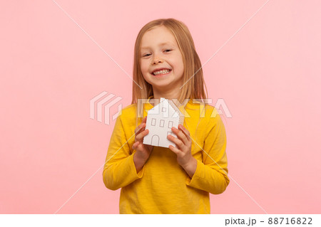 Child dreaming of home. Portrait of happy cute little girl holding paper house and smiling to camera, advertisement of trustworthy real estate agency. indoor studio shot isolated on pink background 88716822