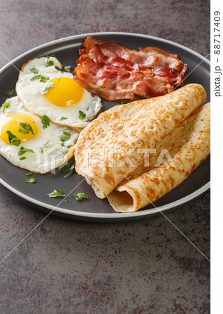 English breakfast of bacon, eggs and oatcakes oat pancakes close-up in a plate. Vertical English breakfast of bacon, eggs and oatcakes oat pancakes close-up in a plate. Vertical 88717409