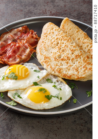 Traditional English Staffordshire oat pancakes, bacon and fried eggs close-up in a plate. Vertical 88717410