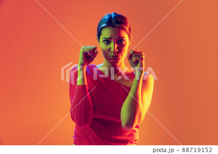 Half-length sad young girl looking offended at camera isolated on peach color background in neon filter. Concept of emotions, beauty, fashion, youth 88719152