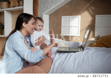 Modern young mother holding her baby daughter greeting her friend or husband on video call on laptop 88722753