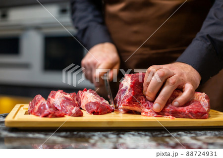 A butcher in an apron in the kitchen cuts pork on a wooden board. Steak. A butcher in an apron in the kitchen cuts pork on a wooden board. Steak. 88724931