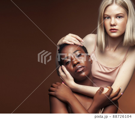 two pretty girls african and caucasian blond posing cheerful together on brown background, ethnicity diverse lifestyle people concept two pretty girls african and caucasian blond posing cheerful together on brown background, ethnicity diverse lifestyle people concept 88726104