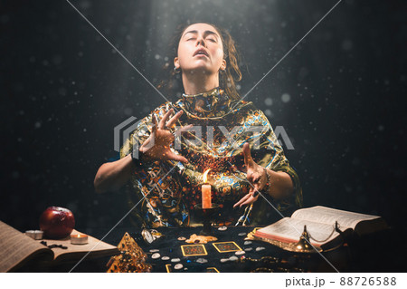 Astrology and divination. Portrait of a fortune teller who reads by candle, eyes closed in ecstasy. Black background. There are magic items on the table 88726588