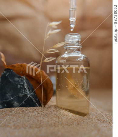 Bottle with a pipette, filled with essence, oil or perfume. Background sand and craft paper. Bottle with a pipette, filled with essence, oil or perfume. Background sand and craft paper. 88728052