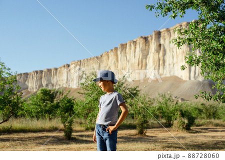 A cheerful kid in jeans, a T-shirt and a blue hat is playing in the garden among the apple trees. 88728060