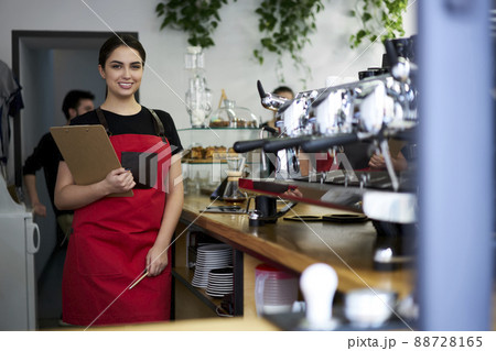 Happy 20s female barista in apron enjoying job at modern coffee shop Happy 20s female barista in apron enjoying job at modern coffee shop 88728165