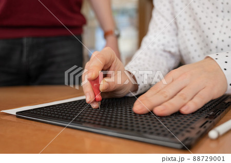 A man teaches a woman how to use a special stencil and stylus to write a letter in Braille. A man teaches a woman how to use a special stencil and stylus to write a letter in Braille. 88729001