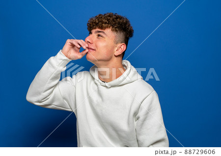 Smiling caucasian young man with hand on mouth looking interested aside at copy space isolated on blue background thinking of shopping opportunities, planning purchases or dreaming concept. 88729606