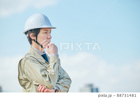 青空を背景に考え事をする作業服姿の若い男性 88731481