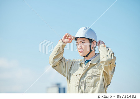青空を背景にヘルメットをかぶる作業服姿の若い男性 88731482