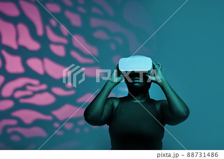 Black young woman in wireless goggles watching virtual reality against the pink pattern background 88731486