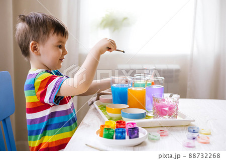 Cute baby boy learning mixing different colors with water and paint in containers. Early development 88732268
