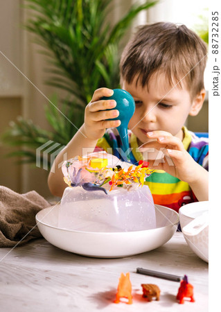 A cute little child pours warm water over toys frozen in ice. Dinosaur defrosting. Early development 88732285