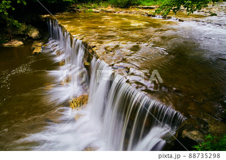 Peaceful waterfalls edge up close flowing into shallow river 88735298