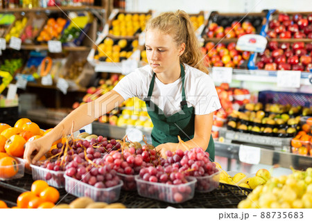 Fifteen-year-old girl who works part-time as a trainee saleswoman puts grapes on the counter 88735683