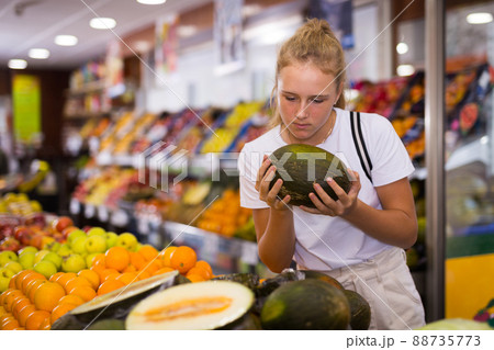 Focused fifteen-year-old girl chooses a ripe melon Focused fifteen-year-old girl chooses a ripe melon 88735773