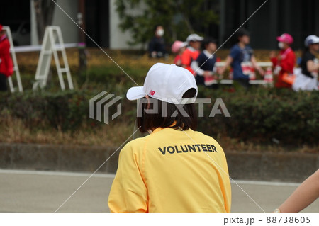 マラソン大会で懸命に走る女性ランナーを見守るボランティア マラソン大会で懸命に走る女性ランナーを見守るボランティア 88738605