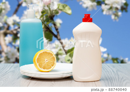 Bottles of dishwashing liquid, plates and lemon. 88740040