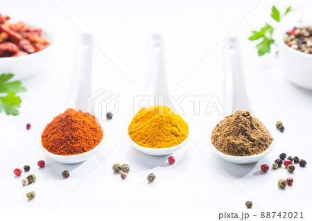 Three white spoons with paprika, turmeric and cumin on a white background. Cooking ingredients and condiments concept. 88742021