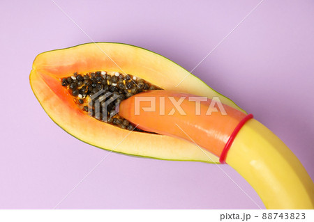 Papaya and banana with condom on violet background 88743823