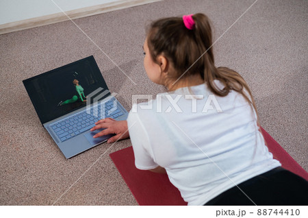 A chubby young woman is watching an online fitness lesson on a laptop. Distance sports training. 88744410