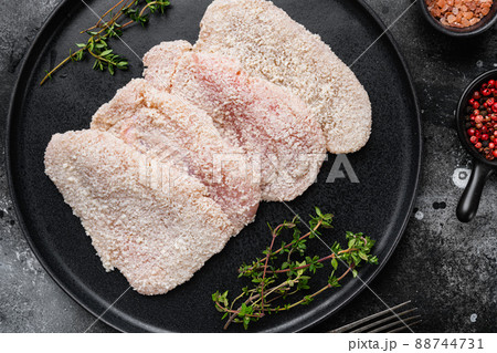 Raw chicken schnitzel in breadcrumbs set, on black dark stone table background, top view flat lay Raw chicken schnitzel in breadcrumbs set, on black dark stone table background, top view flat lay 88744731