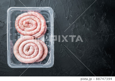 Raw snail sausage in traditional spiral, on black background, in plastic pack, top view flat lay , with space for text copyspace 88747394