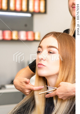 Beautiful young blonde woman with long straight blonde hair getting a haircut at the hairdresser salon Beautiful young blonde woman with long straight blonde hair getting a haircut at the hairdresser salon 88747694